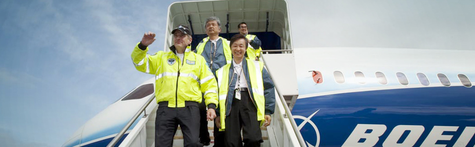 Workers in high visibility vests exiting a Boeing airplane.