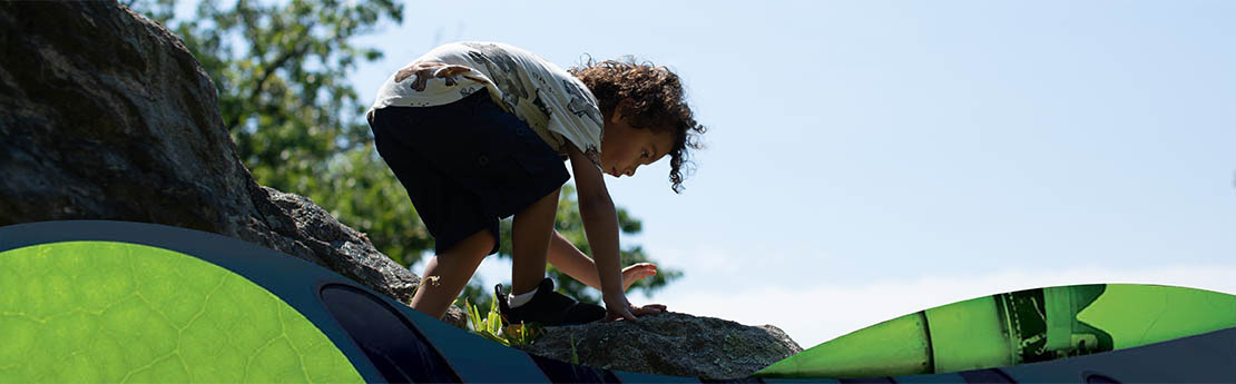 Child playing on a large rock formation with green graphics in foreground.